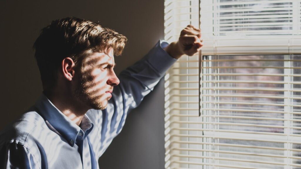 person near clear glass window pane and window blinds low-light photography